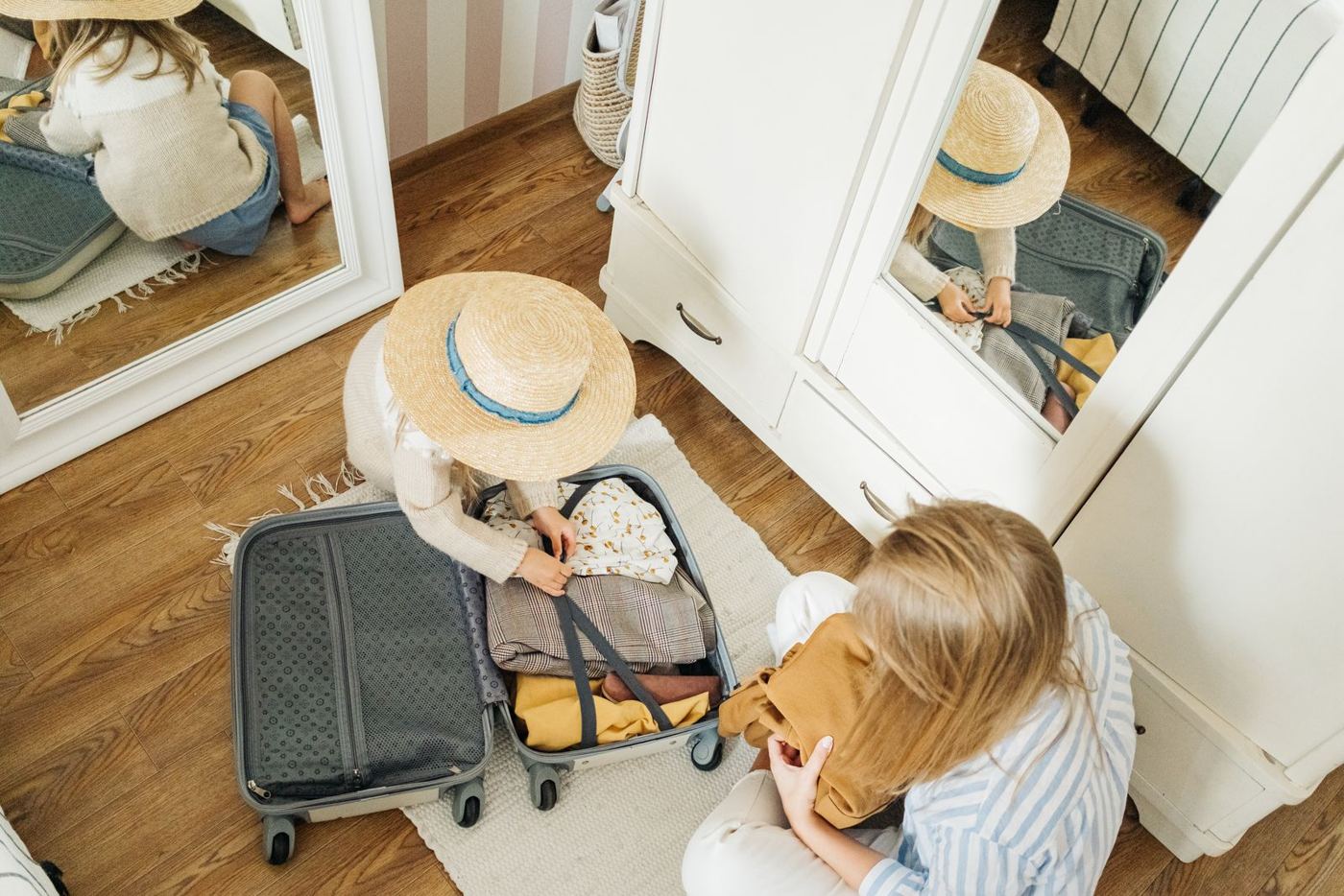 A parent and child packing a small suitcase together on a bed